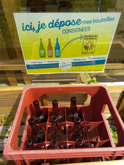 Un casier à bouteilles rempli de bouteilles avec un panneau qui indique « rapportez moi ! »