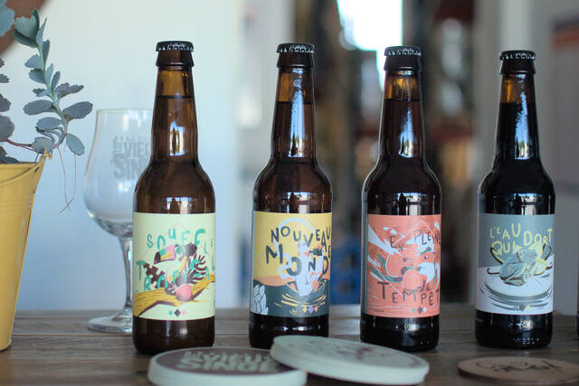 Image de notre gamme de bières. On peut y voir trois bières avec leurs étiquettes, posées sur une table en bois